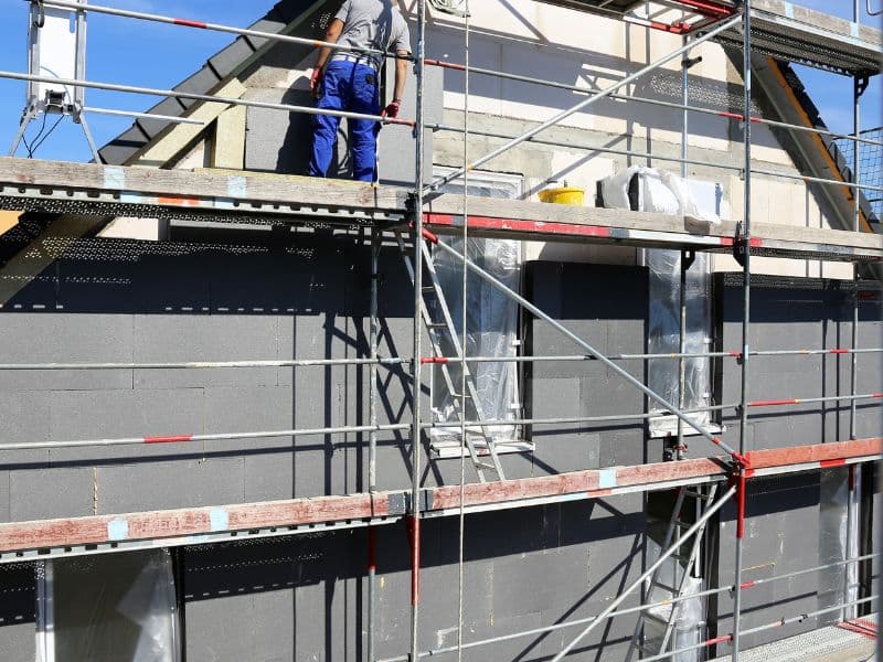 Egy tapasztalt szakember éppen homlokzati hőszigetelést végez a TZ Global tatabányai generálkivitelező cég egyik projektjén. A homlokzati hőszigetelési munkálatok a cég átfogó építőipari szolgáltatásainak részét képezik, amely magában foglalja a teljes körű felújítást, gipszkartonozást, festés-mázolást és egyéb kivitelezési feladatokat. A szakember precíz mozdulatokkal dolgozik, biztosítva a hőszigetelő anyag egyenletes eloszlását és minőségi felületét, amely hozzájárul az épület energiahatékonyságához és tartósságához.